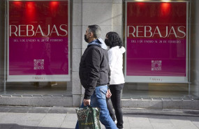 ep dos personas pasan delante de una tienda con carteles de rebajas en una calle comercial del