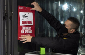 ep un trabajador de hosteleria coloca un cartel donde se lee nos arruinan cerrados sin ayudas