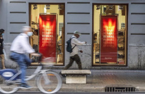 ep varias personas pasan al lado del escaparate de una tienda donde se observan carteles indicativos