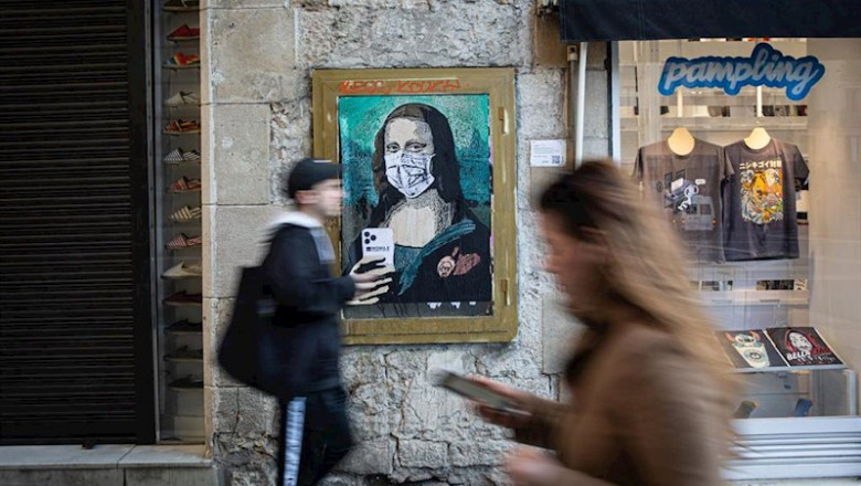 Dos personas pasan con sus móviles junto a una pintura de una Gioconda con un móvil y una mascarilla, obra del grafitero TV Boy llamada 'Mobile World Virus', en referencia a la cancelación del Mobile World Congress a causa del coronavirus, en Barcelona/Ca | David Zorrakino - Europa Press ep ca 20200221172003