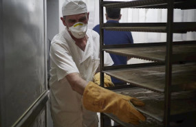 ep un trabajador protegido con mascarilla maneja bandejas para cocer pan en el obrador panaderia