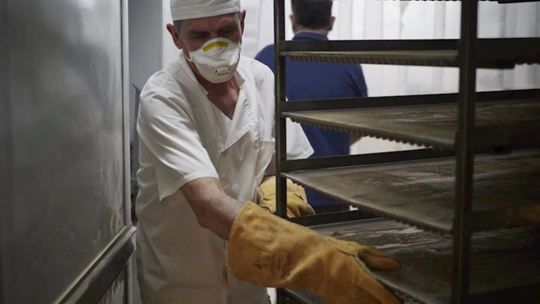 ep un trabajador protegido con mascarilla maneja bandejas para cocer pan en el obrador panaderia